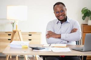 African American businessman smiling relaxed and crossed arms after analysis and research at home office photo