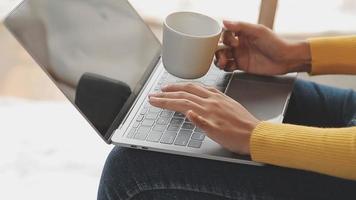 Happy Asian teen girl holding pad computer gadget using digital tablet technology sitting on the couch at home. Smiling young woman using apps, shopping online, reading news, browsing internet on sofa video