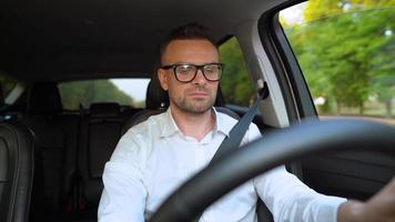 barbu homme dans des lunettes et blanc chemise conduite une voiture dans ensoleillé temps video