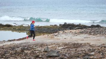 kvinna kör längs de stenig Strand av de hav. friska aktiva livsstil. långsam rörelse video