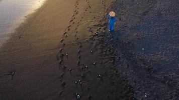 Top view of a girl in a blue dress and hat walking on the beach with black sand, foaming waves of the Atlantic Ocean. Tenerife, Canary Islands, Spain video