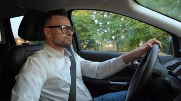 barbu homme dans des lunettes et blanc chemise conduite une voiture dans ensoleillé temps video