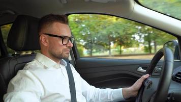 barbado hombre en lentes y blanco camisa conducción un coche en soleado clima video