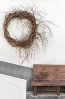 On the wall is a decorative wicker wicker wreath. A gray wall with a dark gray stripe in the background. Below is a wooden bench to sit on. photo