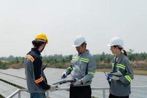 en el techo de un grande solar energía almacenamiento estación edificio un equipo de eléctrico poder ingenieros inspeccionando solar paneles ese tener estado instalado en cientos de hectáreas de campos. foto