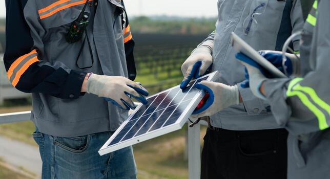 On the rooftop of a large solar energy storage station building, A team of electric power engineers testing a small solar panel that is a prototype installed on hundreds of acres of grassland photo