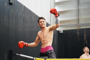 muay tailandés, el marcial Arte de tailandia, boxeador felicidad cuando él gana por en pie en el cuerdas de el boxeo anillo y levantamiento su manos y gritos satisfactoriamente foto