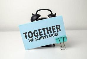 together we achieve more is written in a blue sticker near a black alarm clock photo