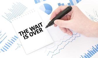 Businessman holding a black marker, notepad with text the wait is over , business concept photo