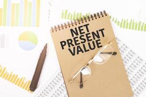 In a craft colour notebook is a net present value inscription, next to pencils, glasses, graphs and diagrams. photo
