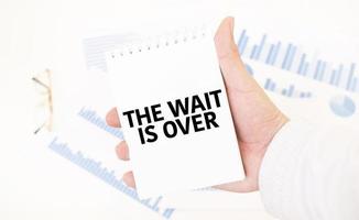 Businessman holding a white notepad with text the wait is over , business concept photo