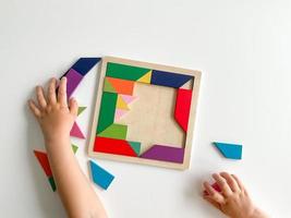 niños mano recoge multicolor de madera mosaico en blanco antecedentes. niño resuelve vistoso tangram foto