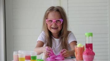 A little girl with glasses is played with a homemade pink slime. Kids hands playing slime toy. Making slime. Copyspace. video