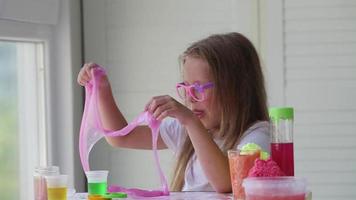 A little girl with glasses is played with a homemade pink slime. Kids hands playing slime toy. Making slime. Copyspace. video