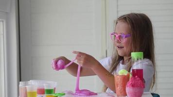 A little girl with glasses is played with a homemade pink slime. Kids hands playing slime toy. Making slime. Copyspace. video