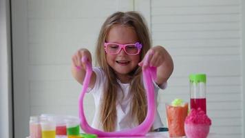 A little girl with glasses is played with a homemade pink slime. Kids hands playing slime toy. Making slime. Copyspace. video