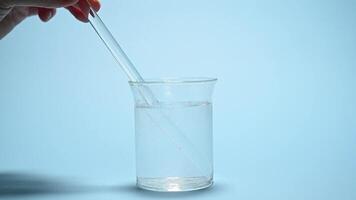 Close-up laboratory stick inside a glass of water with bubbles after dissolving effervescent tablets, isolated over blue color background. Dissolution of fizzy medical pill. Pharmaceutical industry video