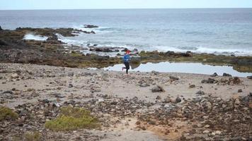 mulher corre ao longo a pedregoso costa do a oceano. saudável ativo estilo de vida. lento movimento video