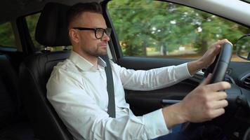 barbado hombre en lentes y blanco camisa conducción un coche en soleado clima video