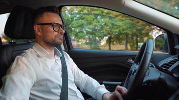 Bearded man in glasses and white shirt driving a car in sunny weather video