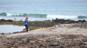 donna corre lungo il pietroso riva di il oceano. salutare attivo stile di vita. lento movimento video