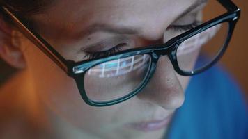 Woman in glasses looking on the monitor and surfing Internet at night. The monitor screen is reflected in the glasses video