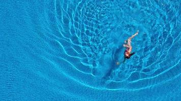 View from the top as a woman in a red swimsuit swimming and lying on her back in the pool. Relaxing concept video