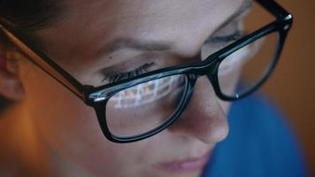 Woman in glasses looking on the monitor and surfing Internet at night. The monitor screen is reflected in the glasses video