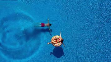 Aerial view of man dives into the the pool while girl is lying on a donut pool float video