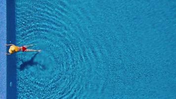 View from the top as a woman in a red swimsuit lying on her back in the pool. Relaxing concept video