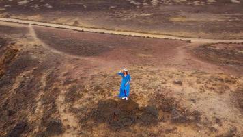 View from the height of woman in a beautiful blue dress and hat stands on top of a mountain in a conservation area on the shores of the Atlantic Ocean. Tenerife, Canary Islands, Spain video