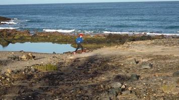 donna corre lungo il pietroso riva di il oceano. salutare attivo stile di vita video