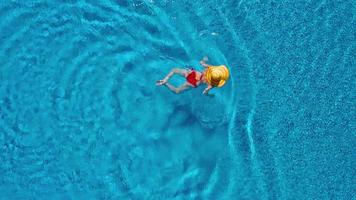 vue de le Haut comme une femme dans une rouge maillot de bain mensonge sur sa retour dans le bassin. relaxant concept video