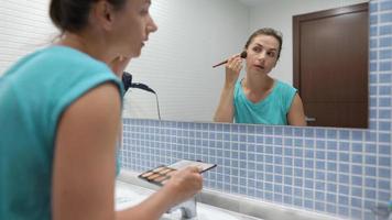 Woman does a morning routine - brushes her teeth, does makeup and puts her hair on video