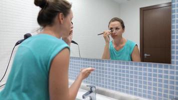 Woman does a morning routine - brushes her teeth, does makeup and puts her hair on video