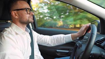 Bearded man in glasses and white shirt driving a car in sunny weather video