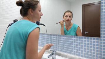 Woman does a morning routine - brushes her teeth, does makeup and puts her hair on video