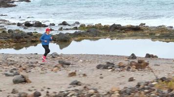 mulher corre ao longo a pedregoso costa do a oceano. saudável ativo estilo de vida. lento movimento video