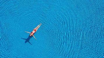 View from the top as a woman in a red swimsuit swimming and lying on her back in the pool. Relaxing concept video