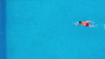 Aerial view of man in red shorts swims in the pool. Slow motion video