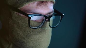 Masculin pirate dans le masque sur visage et des lunettes travail sur une ordinateur dans une foncé Bureau chambre. cybercriminalité concept video