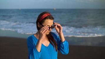 retrato de un mujer en un hermosa azul vestir en un negro volcánico playa. lento movimiento video