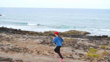 Frau läuft entlang das steinig Ufer von das Ozean. gesund aktiv Lebensstil. schleppend Bewegung video