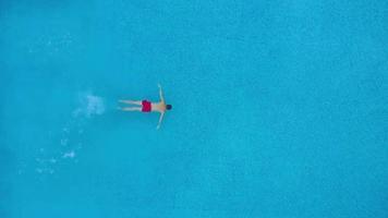 Aerial view of man in red shorts swims in the pool. Slow motion video