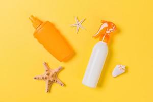 sunscreen cream with starfish and seashells in bottles on yellow background, top view photo