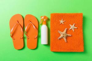Top view of Beach flat lay accessories. sunscreen bottle with seashells, starfish, towel and flip-flop on Colored background with copy space photo