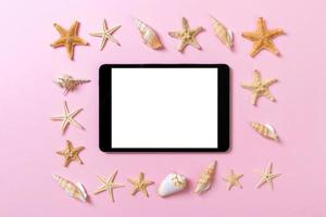 tablet computer with seashells on pink background. technology vacation holidays concept photo