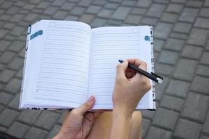 Tender girl's pale hand holding a pen and writing on the blank pages of a notebook. Concept idea of dreaming, planning, motivation, studying. photo