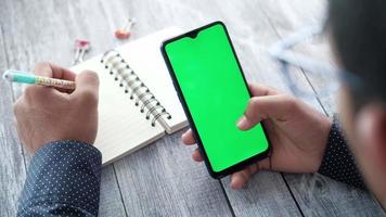 Rear view of young man using smart phone and writing on notepad video