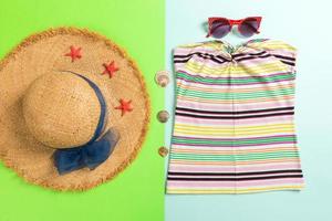 Summer accessories with t-shirt, seashells, sunglasses and straw hat on blue and green background top view flat lay photo